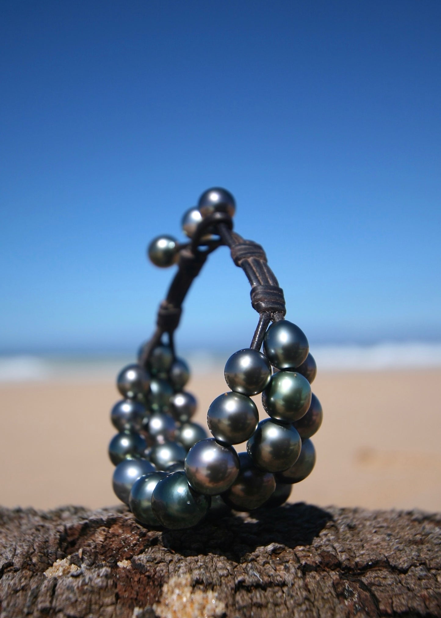 Trésors de St Barth dark Tahitian pearl triple strand bracelet standing on sand with Caribbean ocean behind