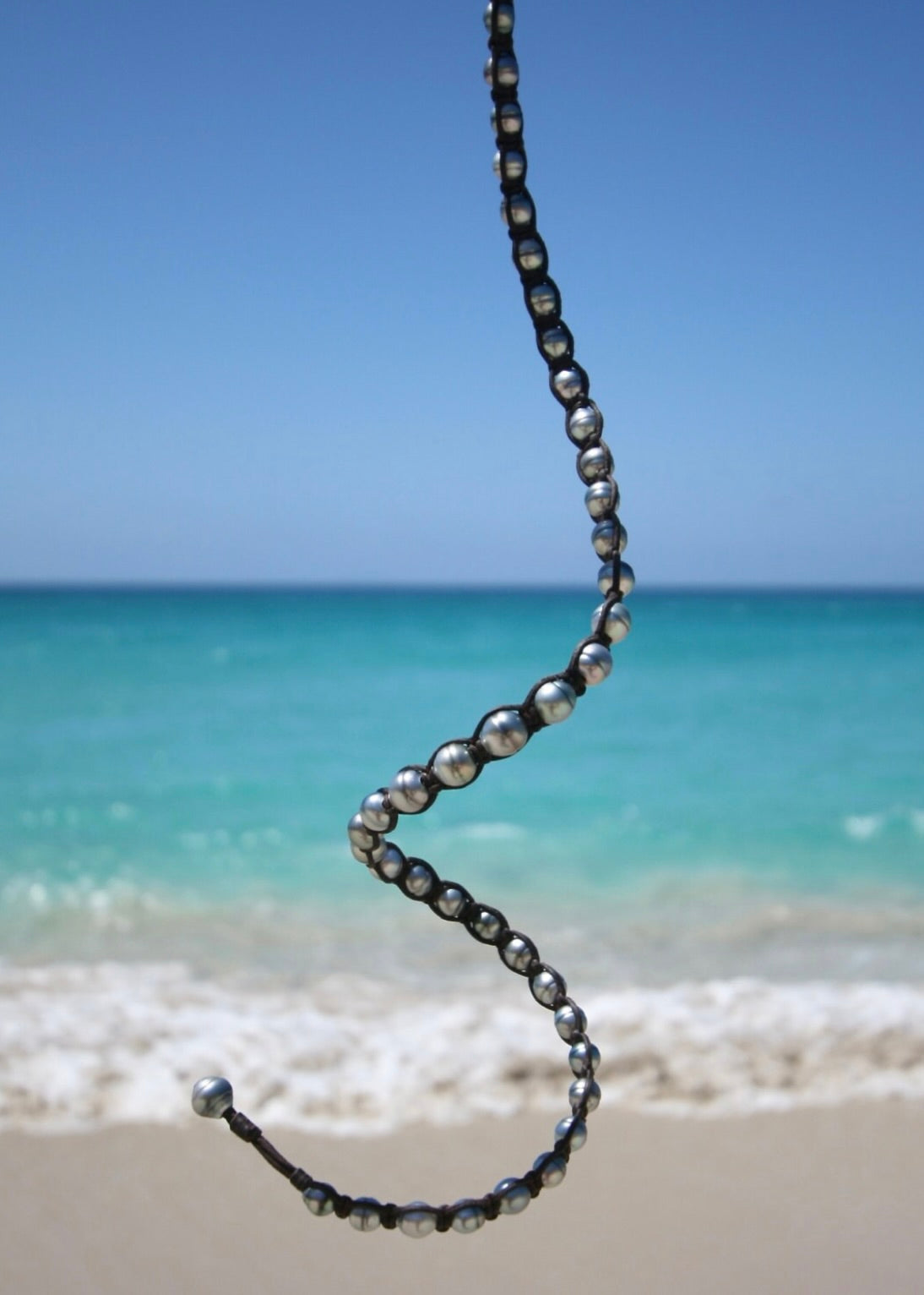 Tahitian silver pearl wrap bracelet draped showing full 49cm length on kangaroo leather with ocean behind