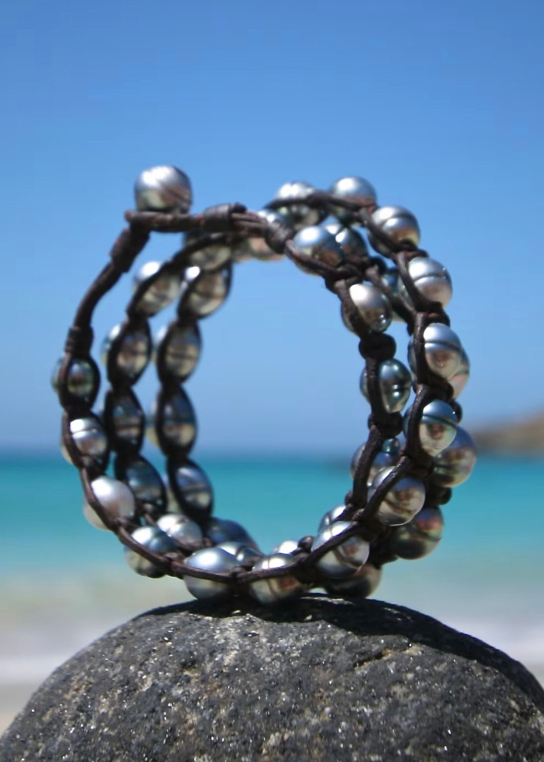 Triple wrap bracelet with 42 Tahitian silver pearls on kangaroo leather standing on stone against blue sky