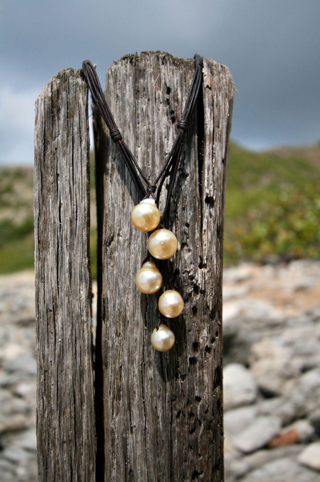 Golden pearl drop pendant necklace on cord hanging on driftwood post, one of a kind jewelry St Barth